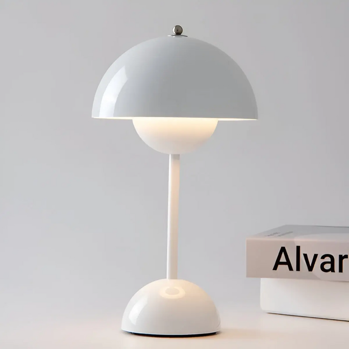 White Scandinavian wireless table lamp displayed on a clean white surface next to a book.