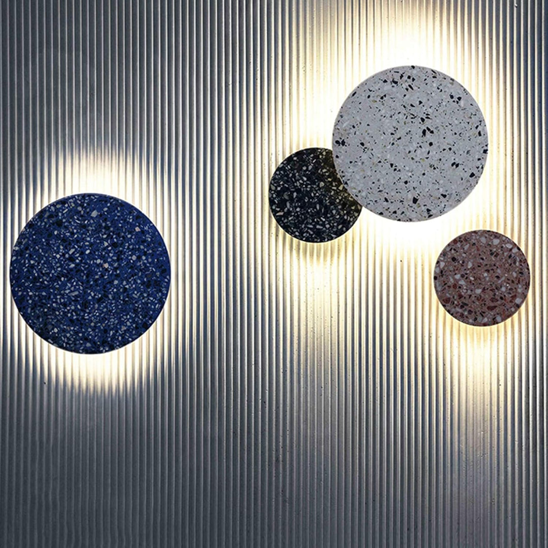 Assorted circular terrazzo wall lamps glowing on a textured wall