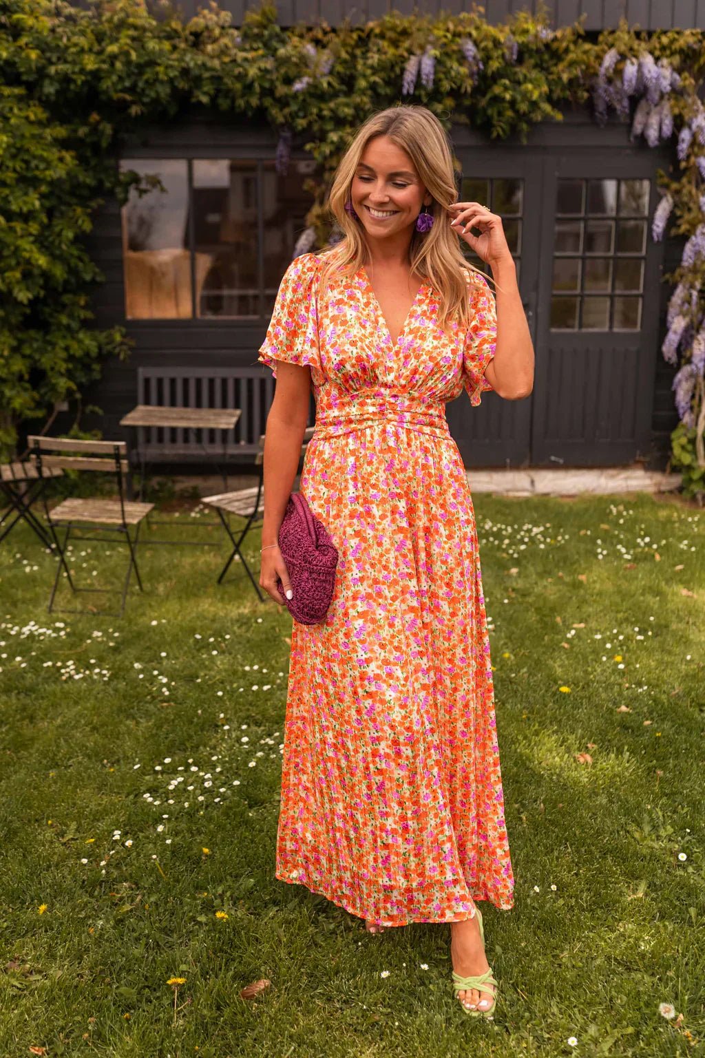 Woman wearing orange floral pleated V-neck maxi dress standing in a garden