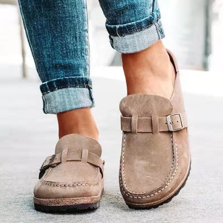 Close-up of beige women's slip-on buckle loafers worn with denim jeans