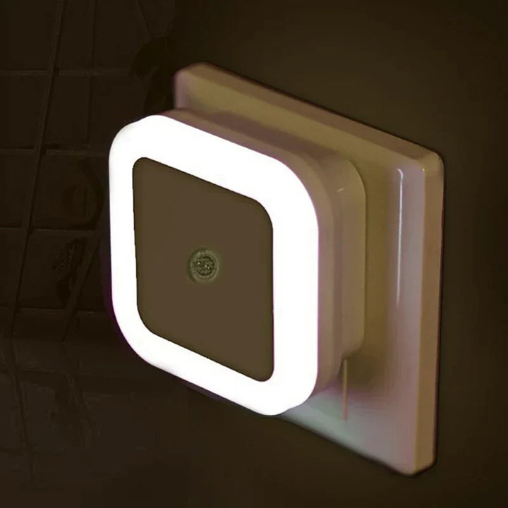 Close-up of square LED night light plugged into a wall outlet emitting a warm white glow