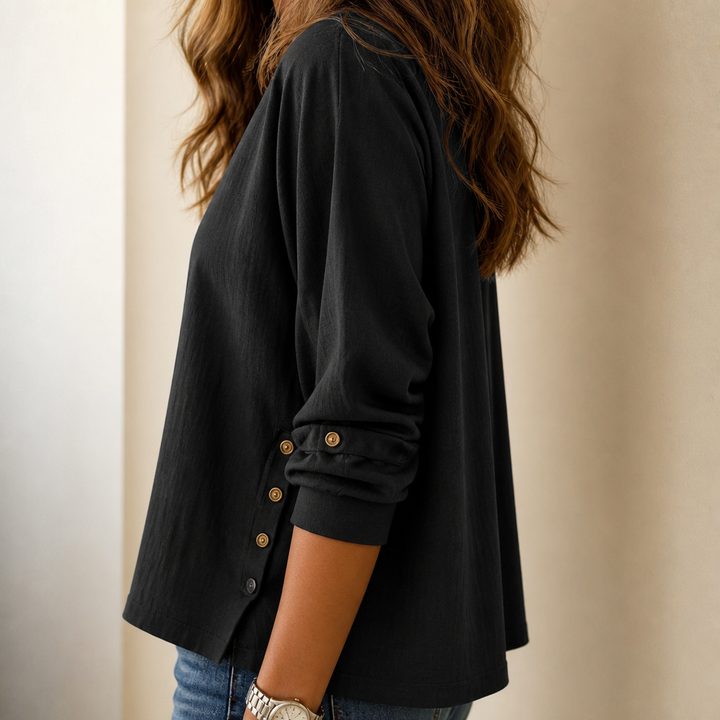 Side profile view of a woman wearing a black long-sleeve top with decorative side buttons