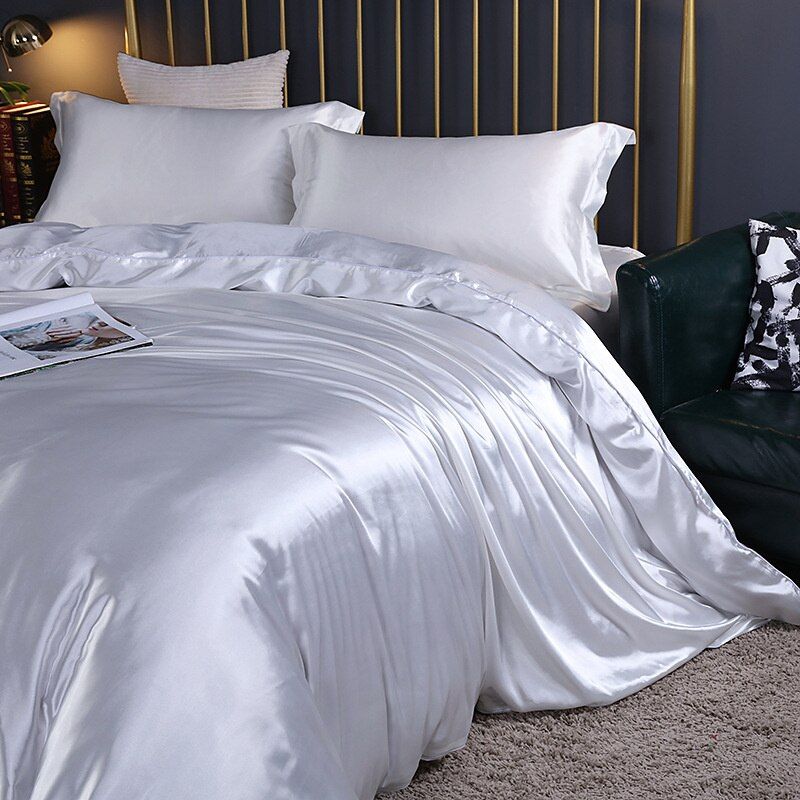 White silk bedding set styled on a bed with a gold headboard
