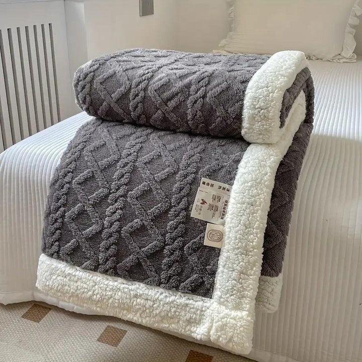 Plush dark gray textured fleece blanket neatly folded on a white bed