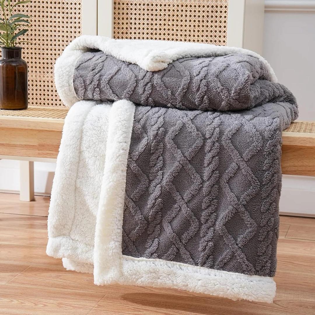 Folded dark gray textured fleece blanket with plush white inner lining displayed on wooden bench