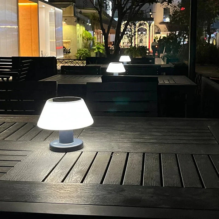 Wireless eco-friendly solar table lamp glowing on a modern outdoor patio table at night.