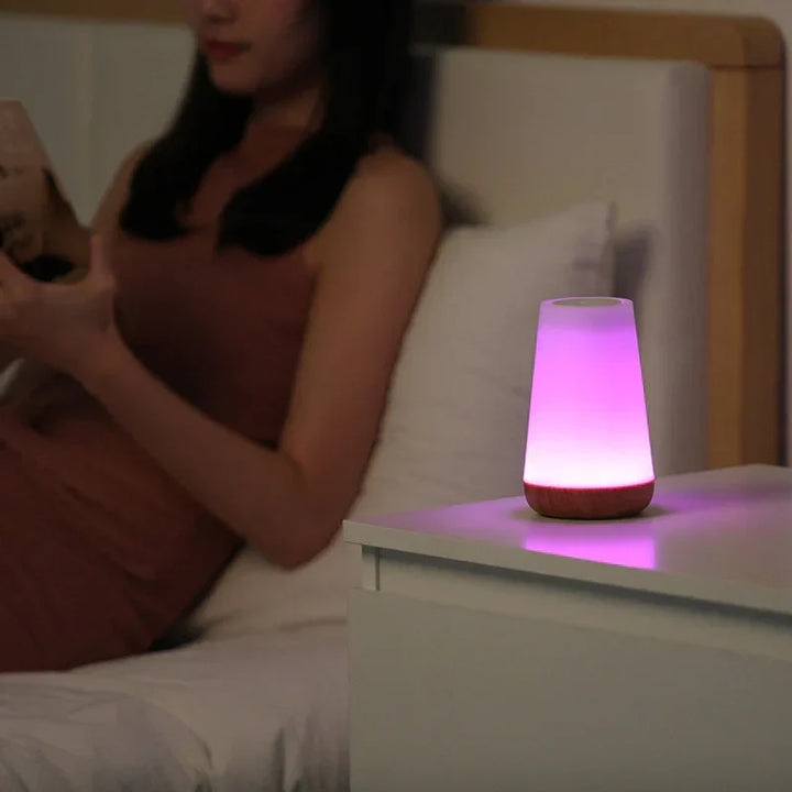 Woman relaxing in bed next to a glowing color-changing night light