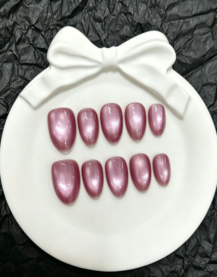 Women's sparkling pink press-on nail set displayed on a white decorative plate with bow