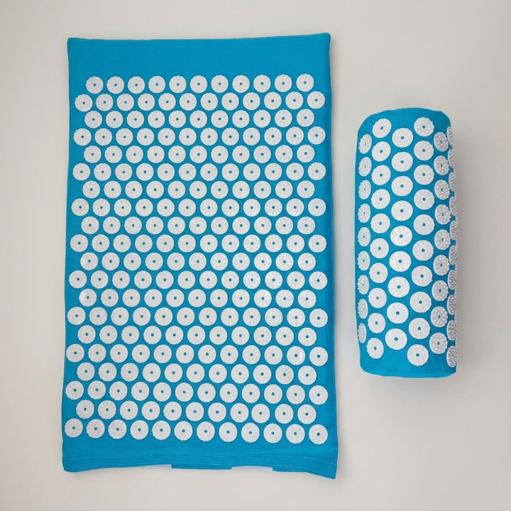 Green acupressure mat and pillow set for back pain relief and muscle recovery on wooden floor