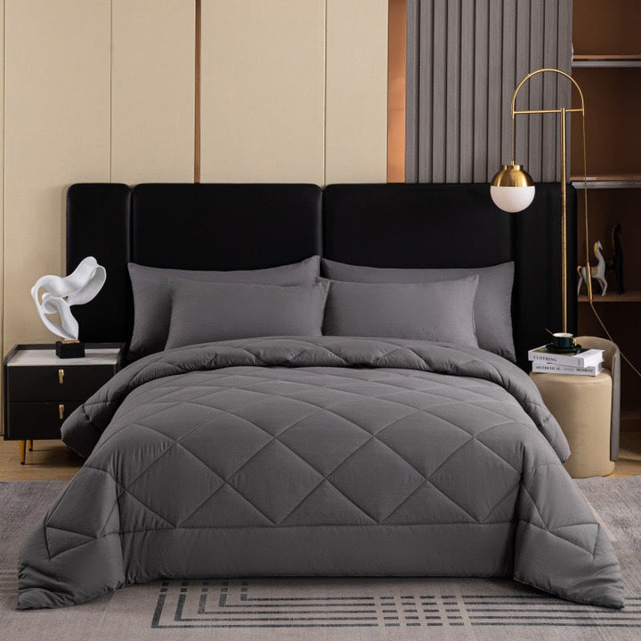 Dark grey quilted comforter set arranged neatly on a bed against a modern headboard