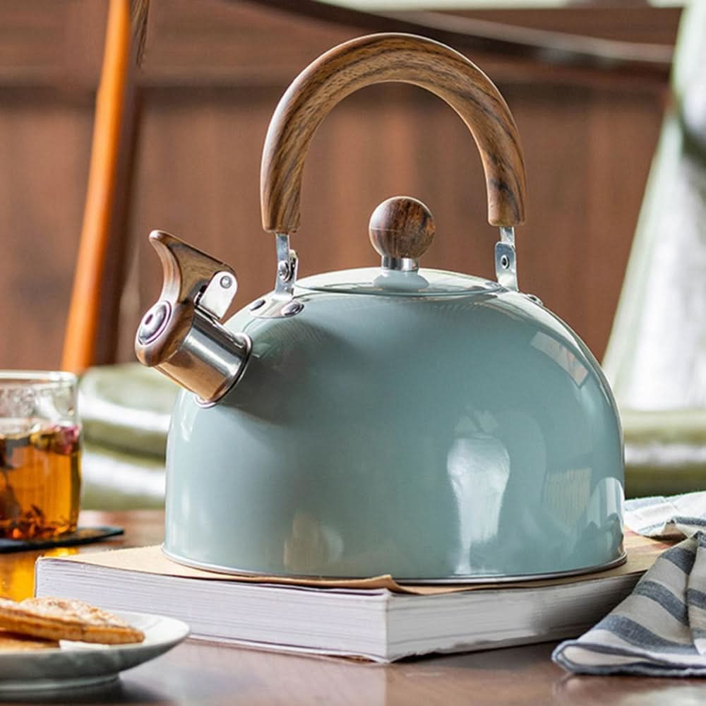 Light green stainless steel whistling kettle resting on a book with a glass of tea nearby