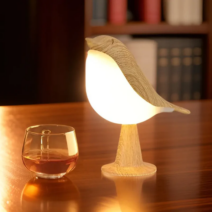 Beige LED bird lamp glowing warmly on a desk next to a glass cup