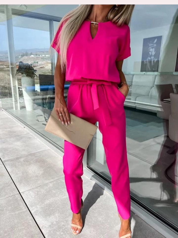 Close-up view of the bright pink v-neck jumpsuit showing the structured waistband and tied belt.