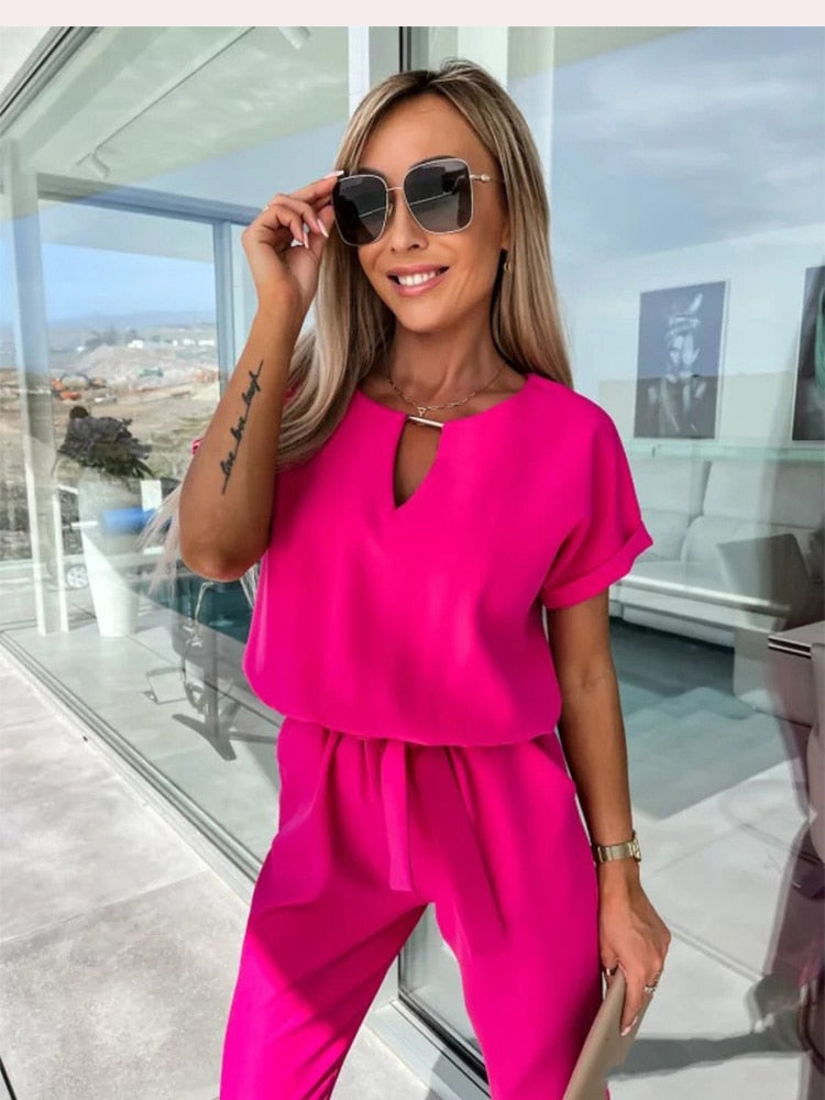 Portrait of a woman wearing the bright pink jumpsuit with sunglasses and a gold necklace.