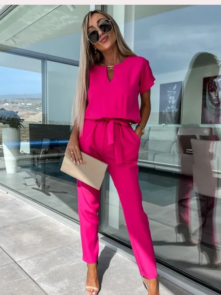 Woman wearing a bright pink stylish v-neck jumpsuit with a waist belt and side pockets outdoors.