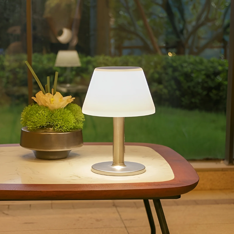Solar energy table lamp glowing softly on an outdoor patio table next to decorative plants