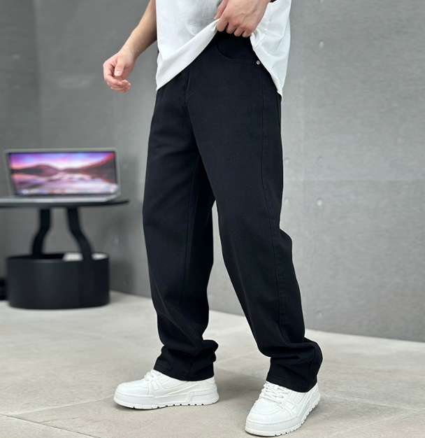 Man wearing black straight leg jeans with slant pockets in a minimalist setting