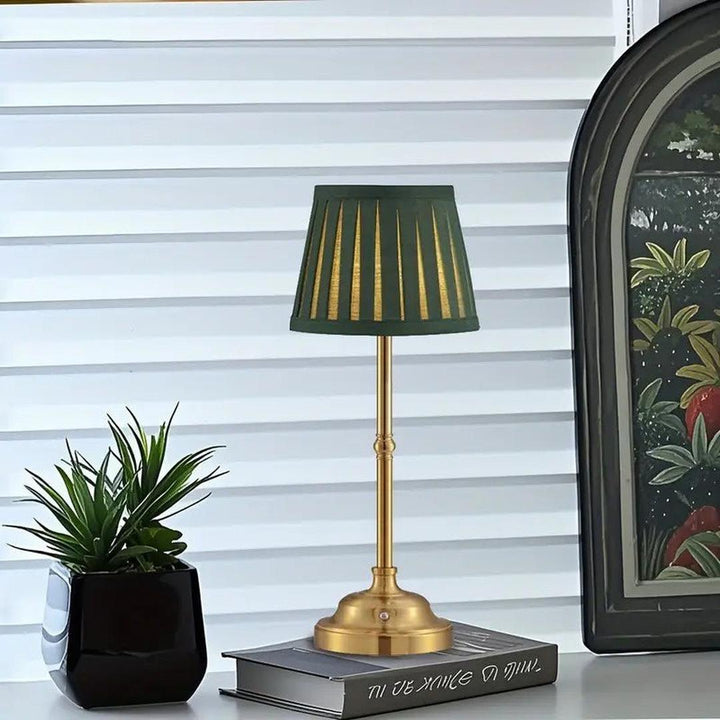 Green table lamp styled on a desk next to books and a potted plant