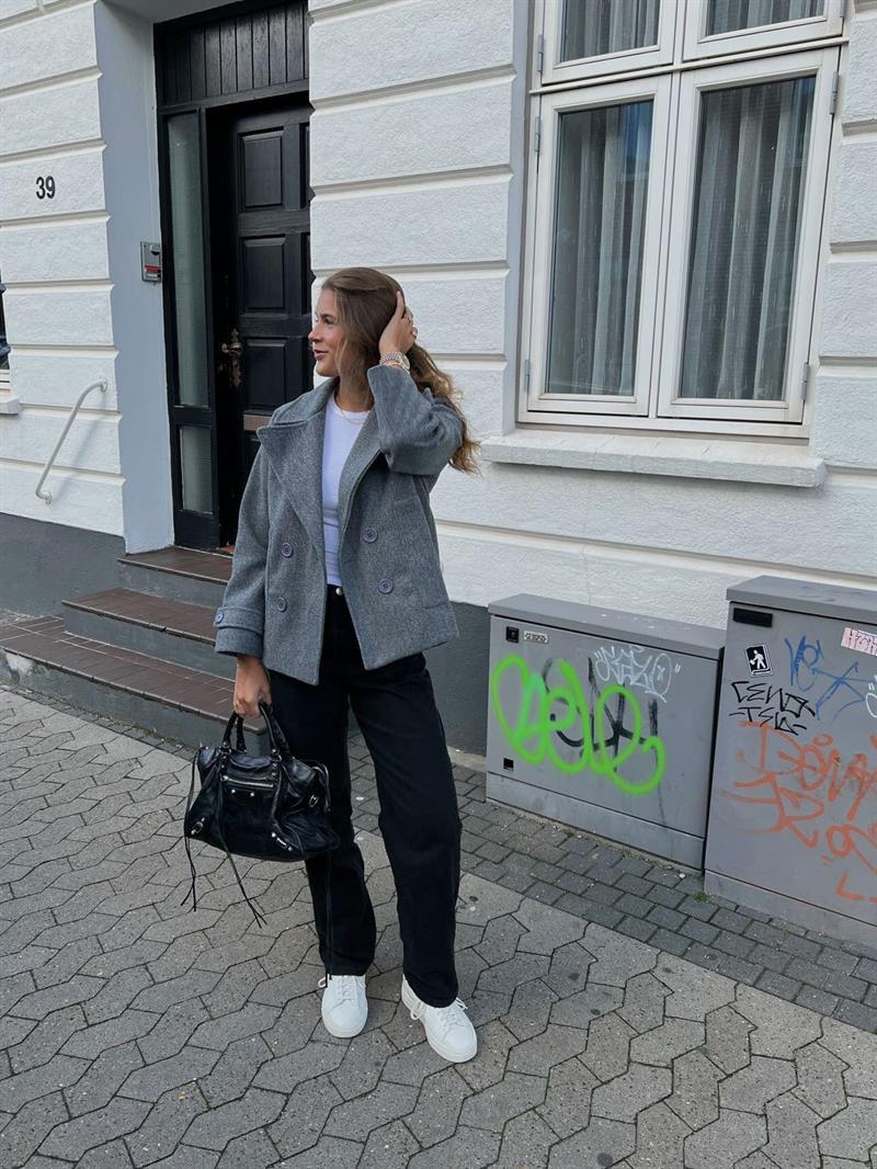 Woman showcasing the grey winter coat paired with black trousers and white sneakers outdoors