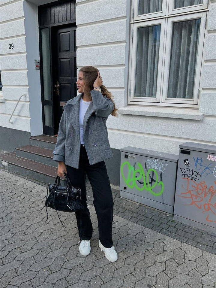 Woman showcasing the grey winter coat paired with black trousers and white sneakers outdoors