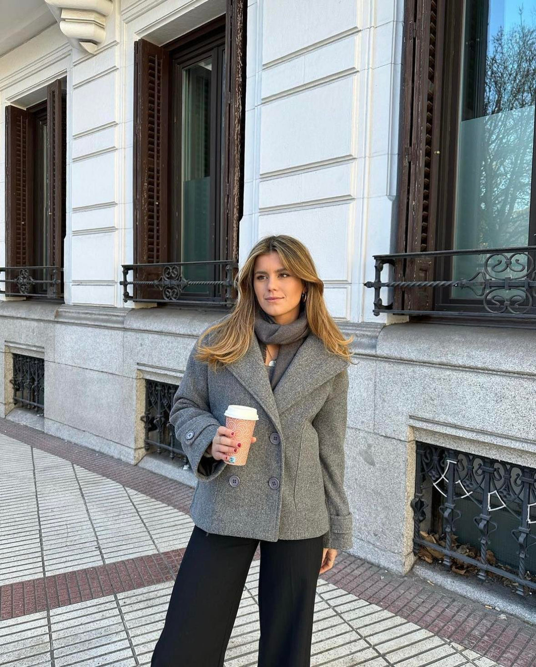 Woman wearing a grey tailored winter coat standing outdoors on a city street