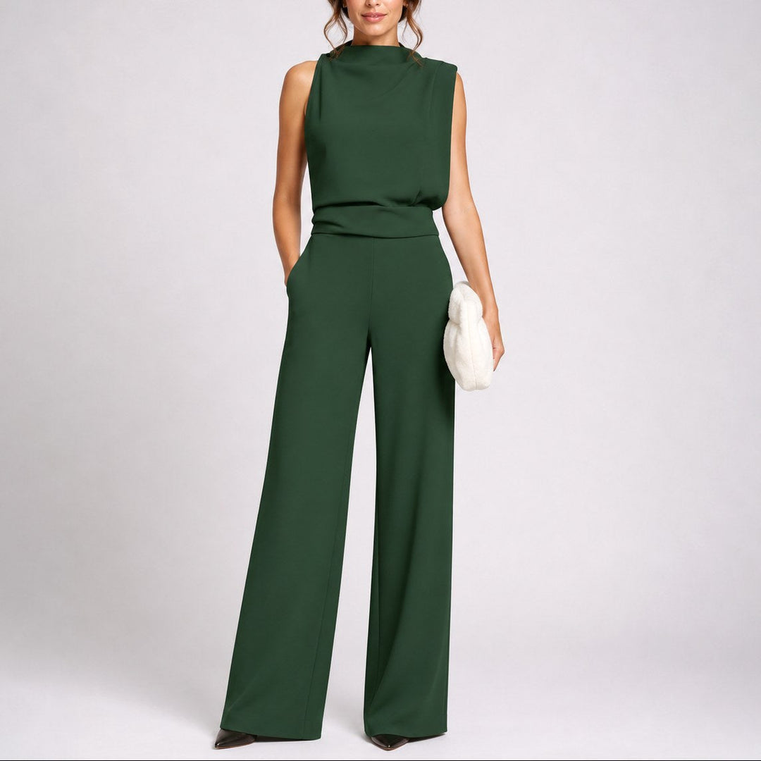 Model wearing dark green sleeveless high neck wide-leg jumpsuit holding white clutch
