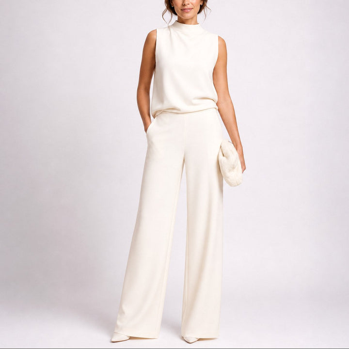 Model wearing white sleeveless high neck wide-leg jumpsuit holding white clutch