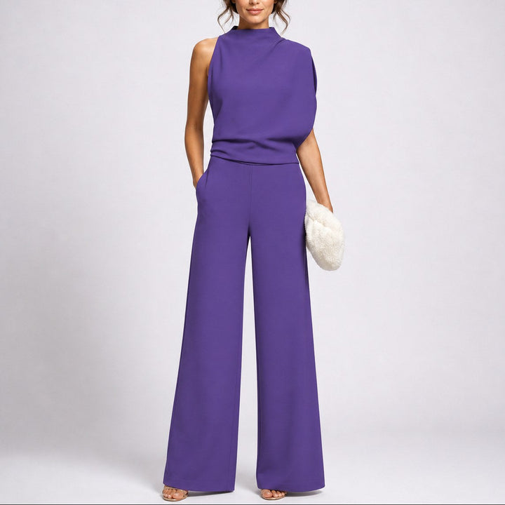 Model wearing purple sleeveless high neck wide-leg jumpsuit holding white clutch