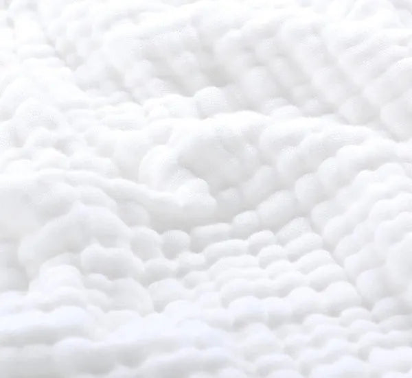 Person wrapped in a soft muslin throw blanket relaxing in a sunlit room