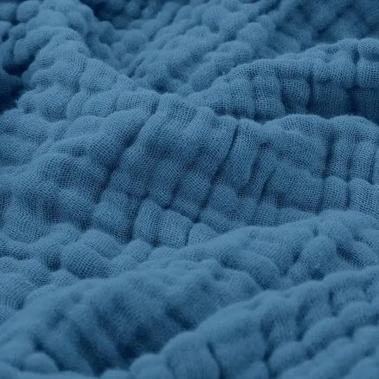 Assorted colors of lightweight muslin blankets stacked on a wooden shelf