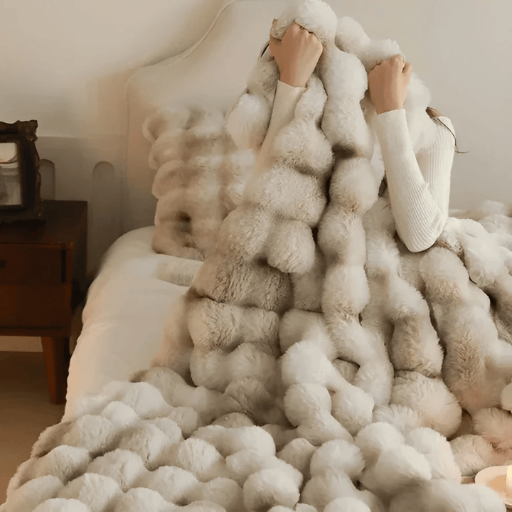 Person wrapped in a plush white thermal fleece blanket in a cozy bedroom setting