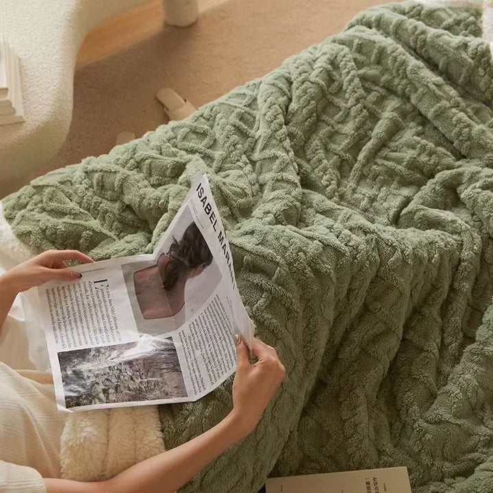 Green winter blanket resting on a bed with a book nearby