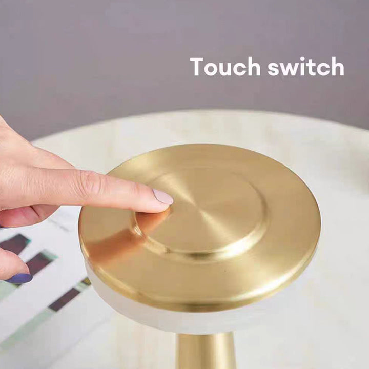 Close-up of a hand using the touch switch on top of the gold LED table lamp.