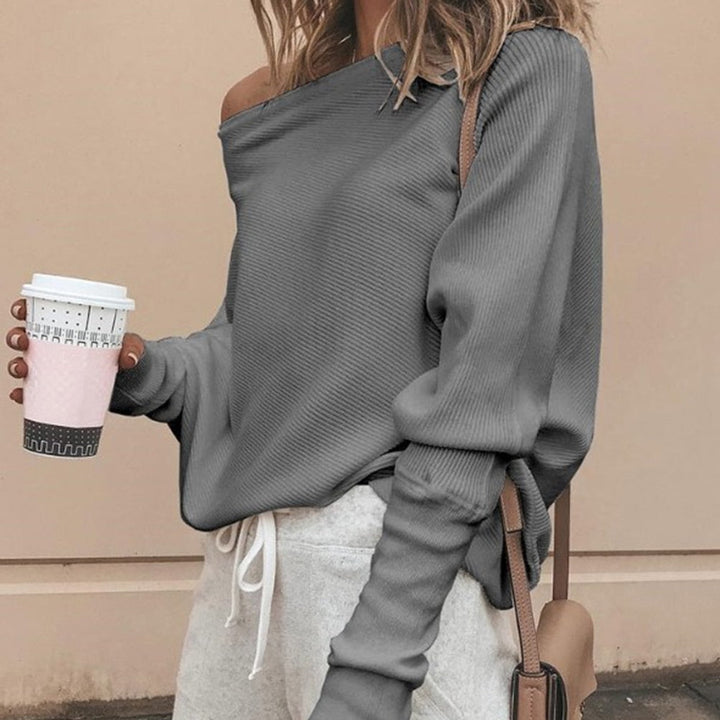 Woman wearing a grey off-shoulder knitted sweater holding a coffee cup