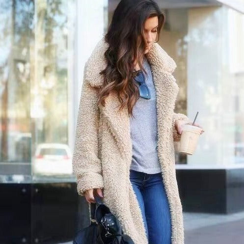 Woman wearing a long apricot teddy fleece coat outdoors holding a drink