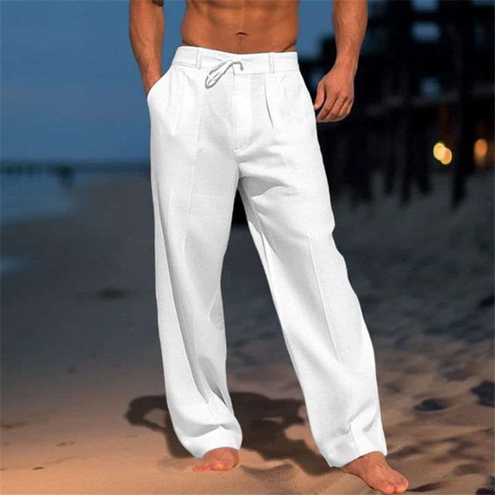 Man wearing white wide leg pleated trousers on a sandy beach