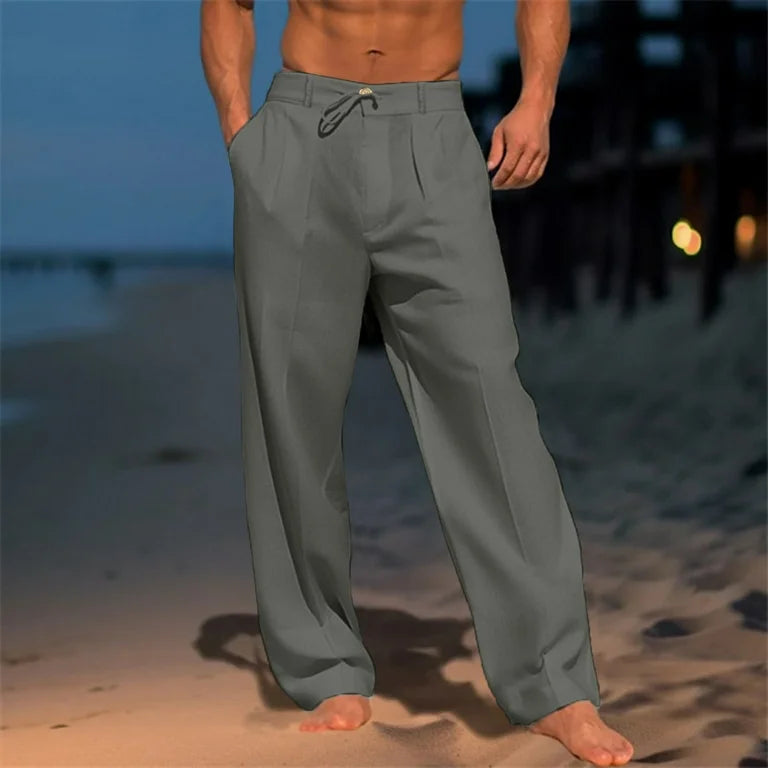 Man wearing grey wide leg pleated trousers on a beach at dusk