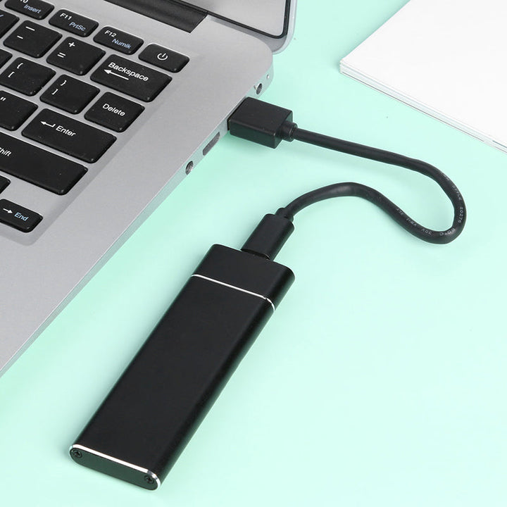 A black portable external solid state drive plugged into a laptop keyboard via a USB cable.