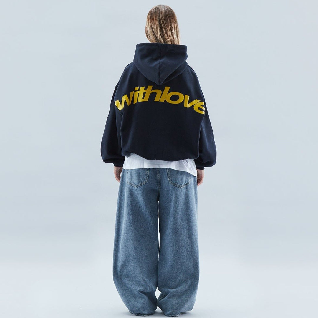 Back view of a woman wearing a navy oversized streetwear hoodie with yellow graphic lettering and wide-leg jeans