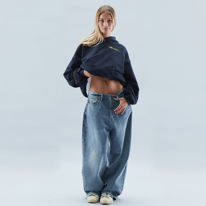 Front view of a woman lifting her navy oversized graphic hoodie showcasing a casual streetwear style