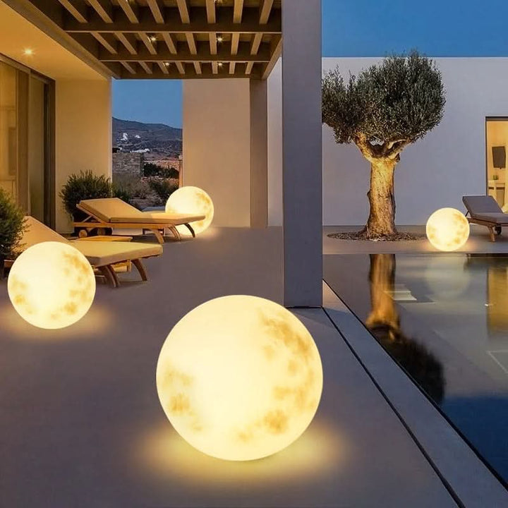 Multiple glowing moon lamps set up on a modern patio near a swimming pool during dusk.
