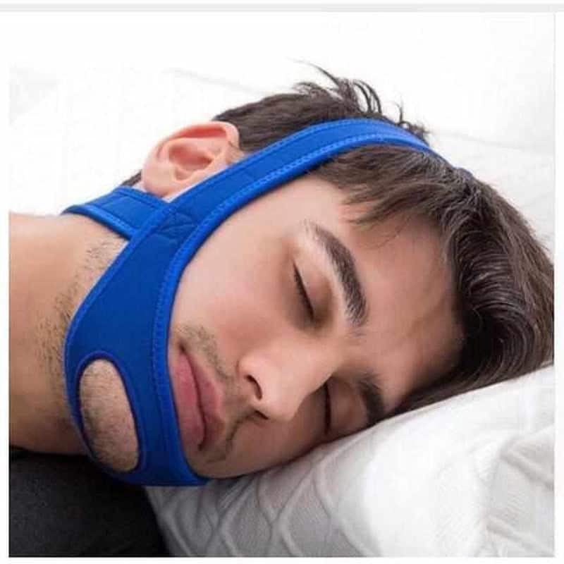 Man wearing a blue anti-snoring chin strap while sleeping on a pillow
