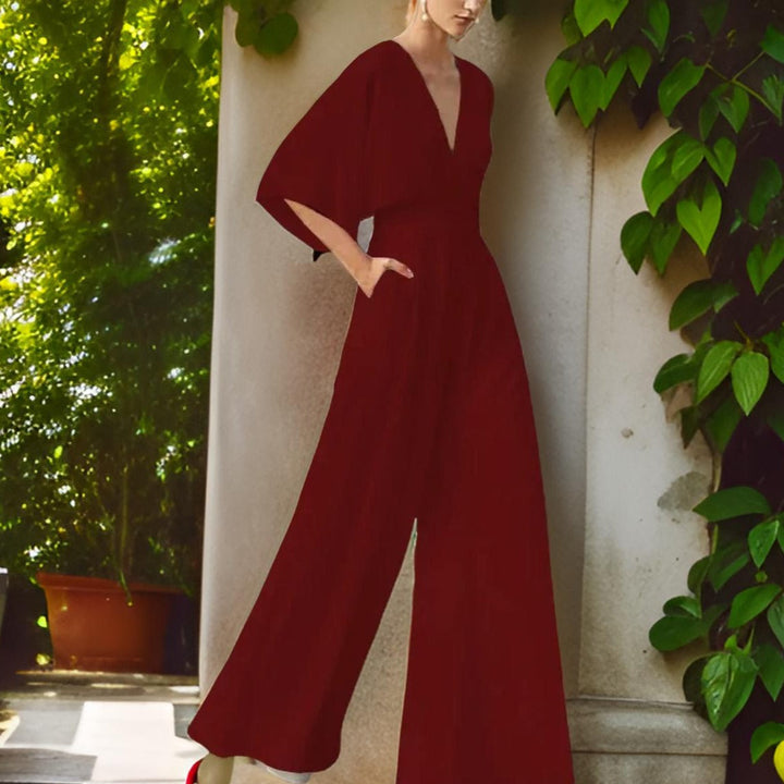Woman wearing a dark red V-neck three-quarter sleeve jumpsuit against a neutral wall