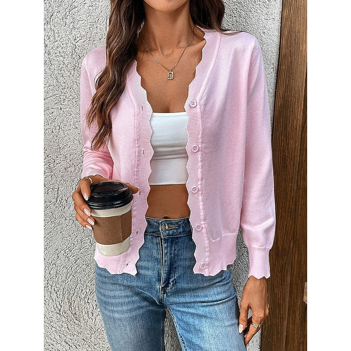 Woman wearing a pink knit cardigan with scalloped trim holding a coffee cup