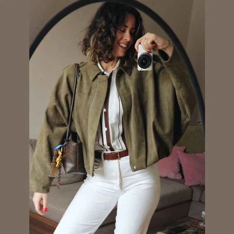 Woman wearing green bomber jacket and white pants in a mirror selfie
