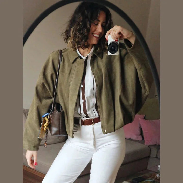 Woman wearing green bomber jacket and white pants in a mirror selfie