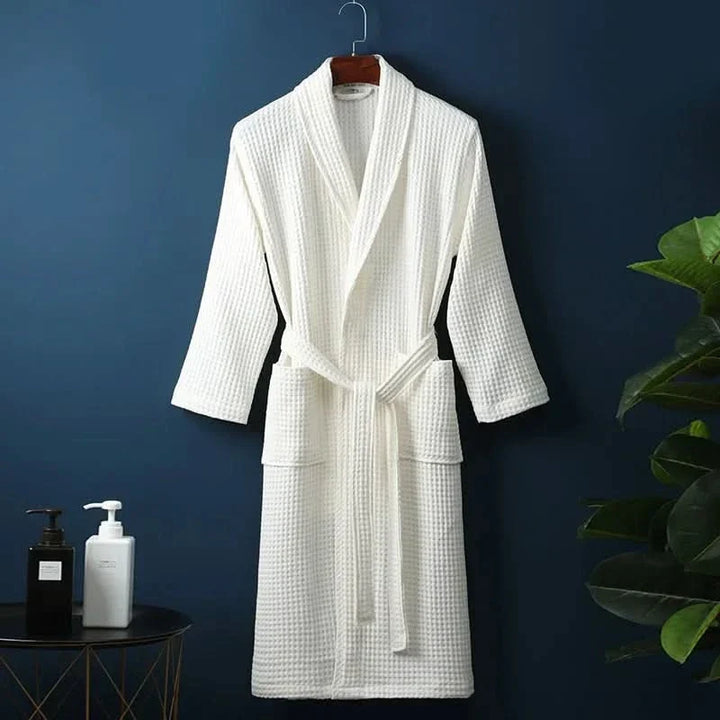 White unisex waffle bathrobe hanging on a hook against a dark blue wall