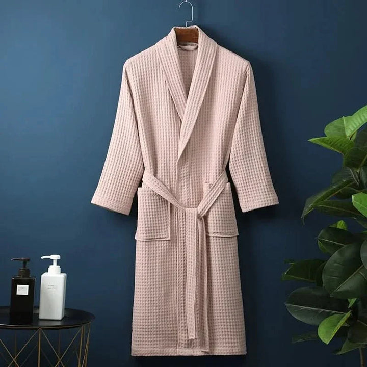 Pink unisex waffle bathrobe hanging on a hook against a dark blue wall