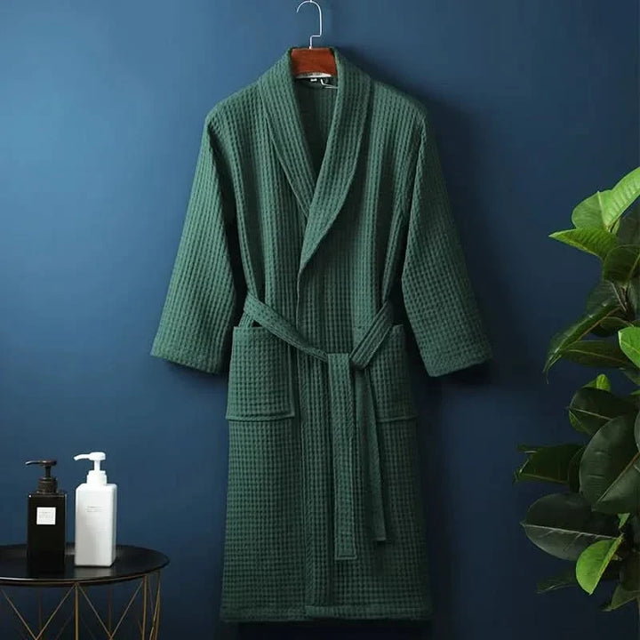 Green unisex waffle bathrobe hanging on a hook against a dark blue wall