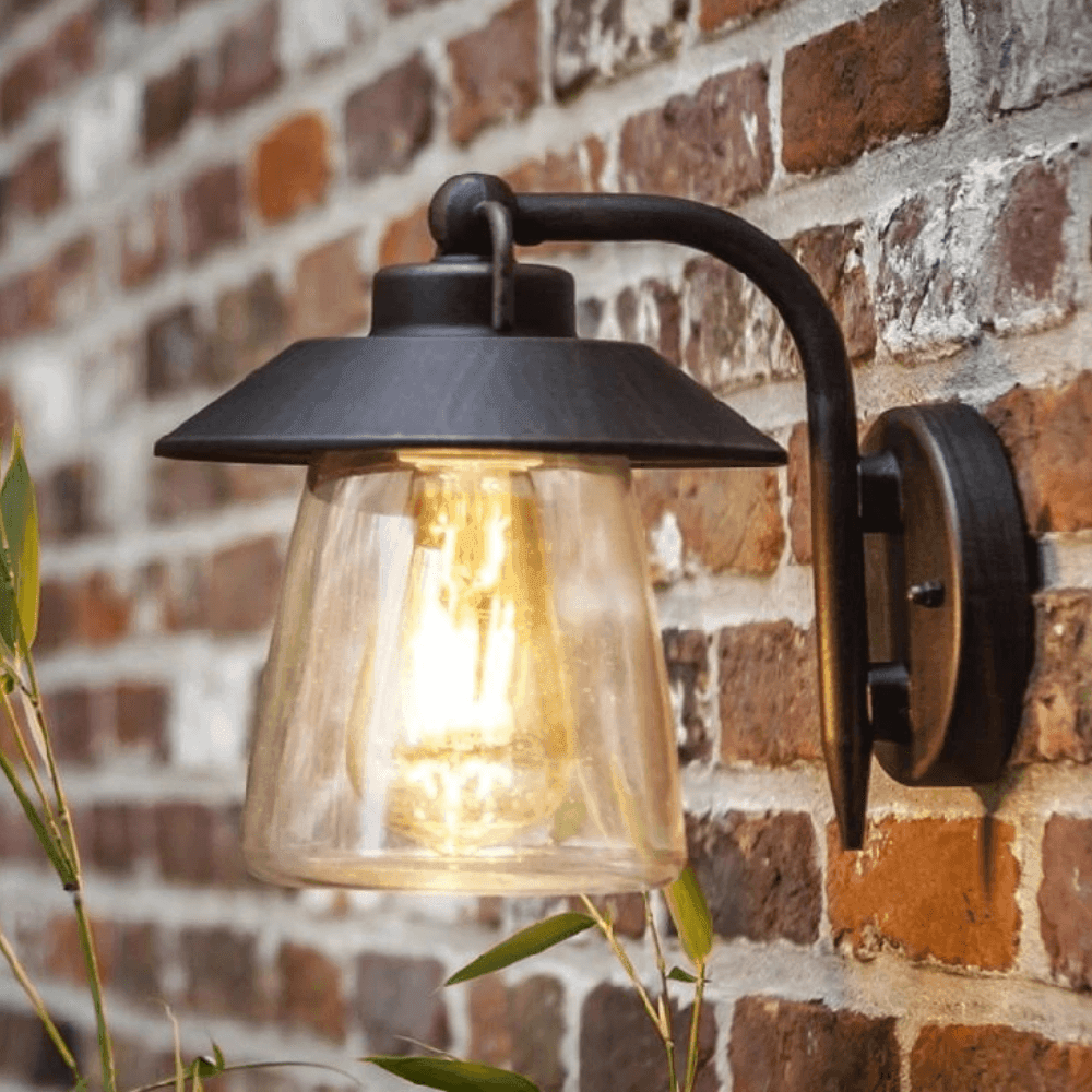 Close-up of black metal and glass outdoor wall lamp mounted on a brick wall with warm lit bulb